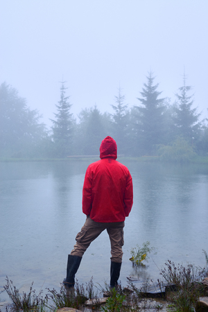 Rear view of tourist in red waterproof jacket looking at lake in the morningの写真素材