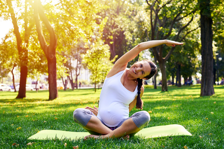 Closeup of pregnant woman in good shape stretching on yoga mat outdoorsの写真素材