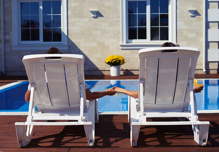 Rear view of couple relaxing in front of modern house near poolの写真素材