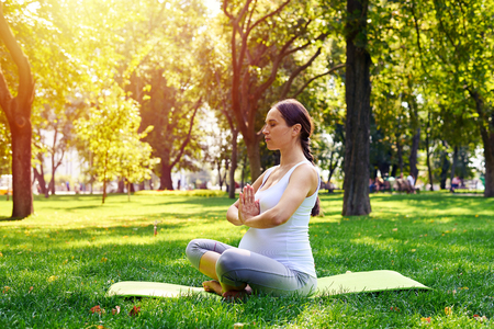 Side view of adorable pregnant woman sitting in lotus pose and relaxing in parkの写真素材