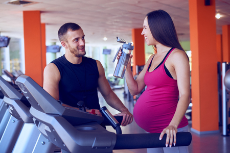 Closeup of pregnant woman drinking water while speaking to personal trainer in gymの写真素材