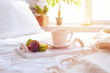 Closeup of yummy macaroons with a cup of tea on tray, standing on bedの写真素材