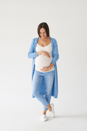 Full-length shot of elegant woman looking at pregnant belly in studioの写真素材