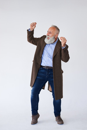 Full-length shot of handsome mature bearded in coat having fun in studioの写真素材