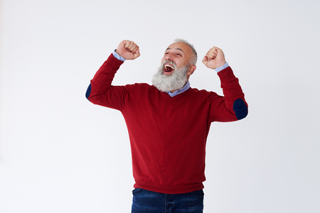 Closeup of happy mature bearded man raising hands looking upwards, celebrating victoryの写真素材