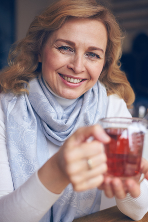 Vertical of beautiful mature woman holding a cup of tea in handsの写真素材