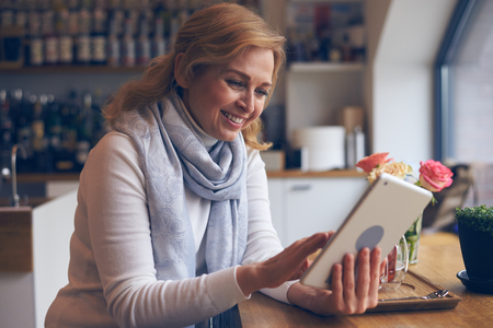 Closeup of smiley mature woman using digital tablet in cafeの写真素材