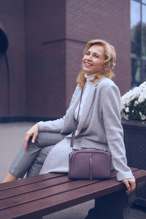 Vertical of cheerful mature woman looking upwards while sitting on the benchの写真素材