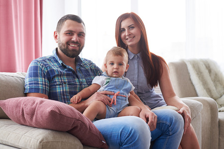 Closeup of happy smiling family of three sitting on sofa looking at cameraの写真素材