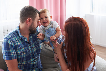 Closeup of young couple with pretty daughter laughing on sofaの写真素材