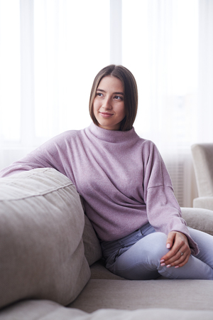 Closeup of girl wearing cozy sweater sitting on sofa at home, enjoying leisure timeの写真素材