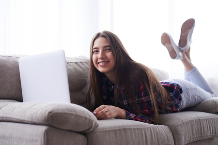 Closeup of relaxed girl lying on sofa with laptop, surfing netの写真素材