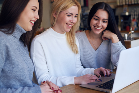 Side view of three women having good time while sitting around a laptop at cafe