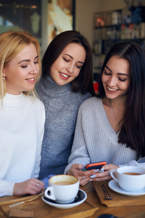 Vertical of woman showing something on smartphone to two friendsの写真素材