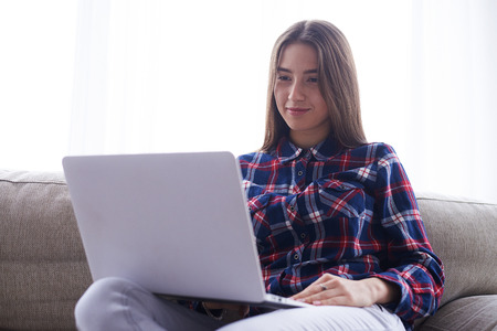 Closeup of girl holding netbook on hips while sitting on sofa. Home interior, cosy atmosphereの写真素材