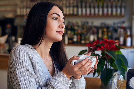 Side view of dreamy girl holding cup of coffee a cafeの写真素材