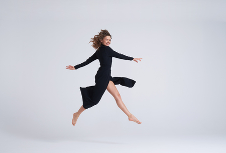 Full-length shot of young attractive woman in black dress jumping in the airの写真素材