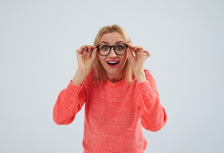surprised blond in sweater holding glassesの写真素材