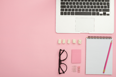 Feminine work desk of orderly person with laptop, glasses, jotteの写真素材