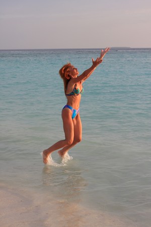 The beautiful, harmonous girl jumps in water at a beach edgeの写真素材