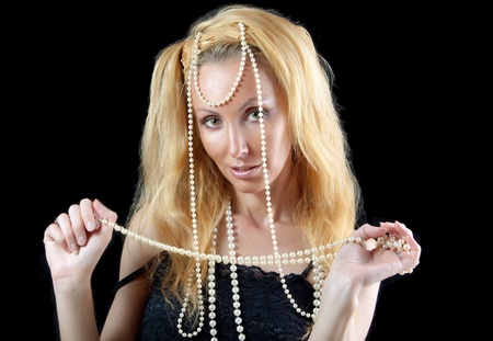 beautiful young blonde woman with long hair and a pearl beads on dark background.の写真素材