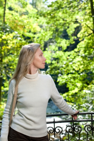 The beautiful woman in a white sweater on the bank of the lake against bright green foliage

の写真素材