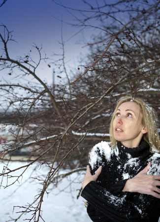 The young frozen woman stand under the falling snow under a tree.の写真素材