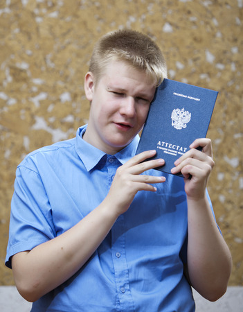 schoolboy with the certificate about completion of education at school, upset from parting with schoolの写真素材