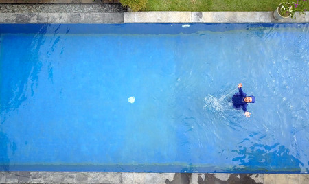 attractive woman in a Muslim swimwear burkini splashes water in the pool, flat lay, view from drone