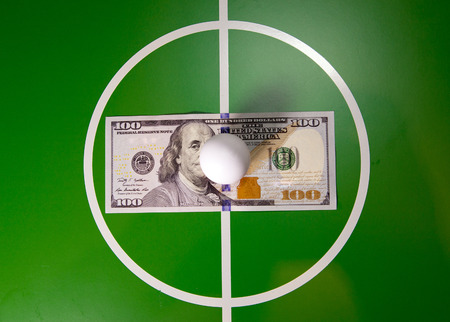 RUSSIA - AUGUST 12, 2015: Toy soccer ball in a midfield, in the center of the green fieldand the banknote in hundred dollarsの写真素材