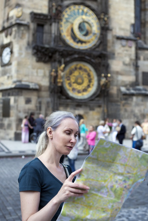 the woman watches the map of the city on background of historical medieval astronomical Clock on the Old Town Hall in Prague, Czech Republicの写真素材