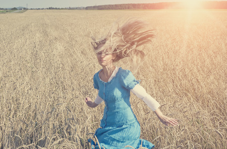 The beautiful woman in a blue long dress in the field of ripe ears of cereals, retro effectの写真素材