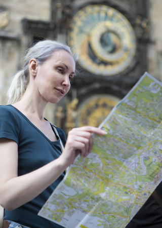 the woman watches the map of the city on background of historical medieval astronomical Clock on the Old Town Hall in Prague, Czech Republicの写真素材