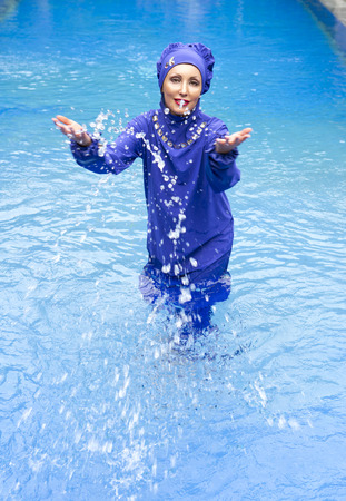 attractive woman in a Muslim swimwear burkini splashes water in the poolの写真素材