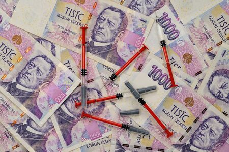 Czech money scattered on which are laid syringe.