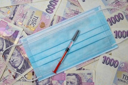 Medical mask laid on Czech money. Syringes are placed on the veil. The label "Antiviral" is placed on the syringe.の写真素材