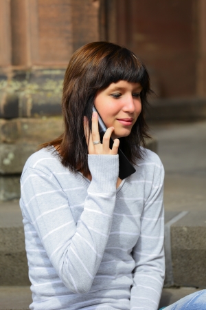 Portrait of a young woman with mobile phone in background a sandstone  wall, outdoor in a small city Dillingen / Saarland / Germanyの写真素材