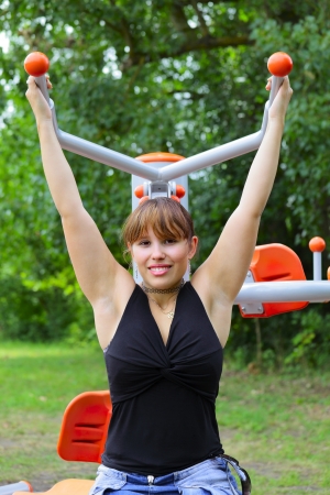 A young woman sitting on sport device and laughs in the pause between sport exercises. Outdoor in park in city Saarlouis, Saarland / Germany.の写真素材