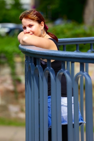 A young woman stands on a bridge railing, in background green blur leaves, outdoor in a small city Saarlouis / Saarland / Germany.の写真素材