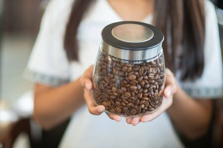 A hand holding a jar of roasted coffee beansの写真素材
