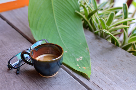 A cup hot espresso coffe with glasses and green leaf on wood tableの写真素材