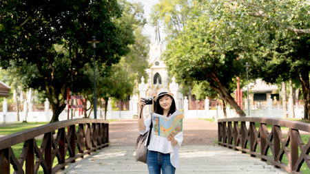 Young Asian woman traveler holding photo camera and map on bridge backgroundの写真素材