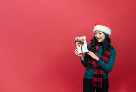 Young lady wiht santa hat and holding Christmas gift isolated red background. Emotion smile. Event x-mas / valantineの写真素材