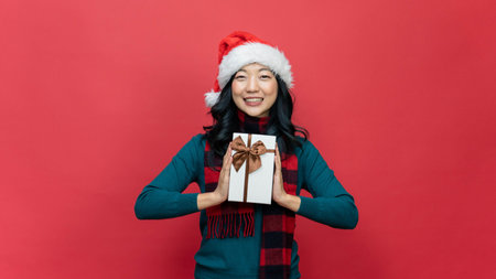 Smiling woman hold red gift box isolated over red background. Concept of the New Year and Christmas Day.の写真素材