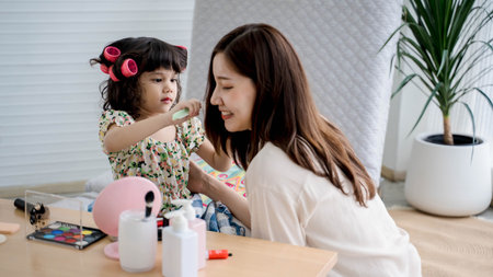 Little girl playfully applying makeup on her smiling mother, spending quality time together at home...