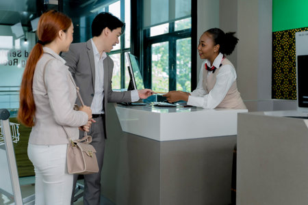 Friendly airline staff assisting a business couple at check-in counter with boarding pass and...