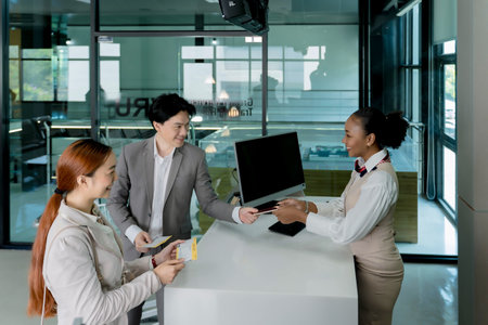 Business travelers handing passport to smiling airline staff at check-in counter inside airport terminal before international flight boarding processの写真素材
