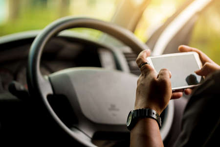 Man hand holding mobile phone and pointing empty touch screen during driving. People in car playing smartphone during traffic jam.の写真素材