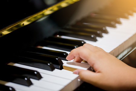 Boy play the piano with selective focus to piano key and hands. There are musical instrument for learning music.の写真素材