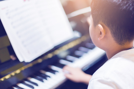 Blurry picture of boy play the piano with selective focus. hands playing piano with music notation. There are musical instrument for learning music.の写真素材
